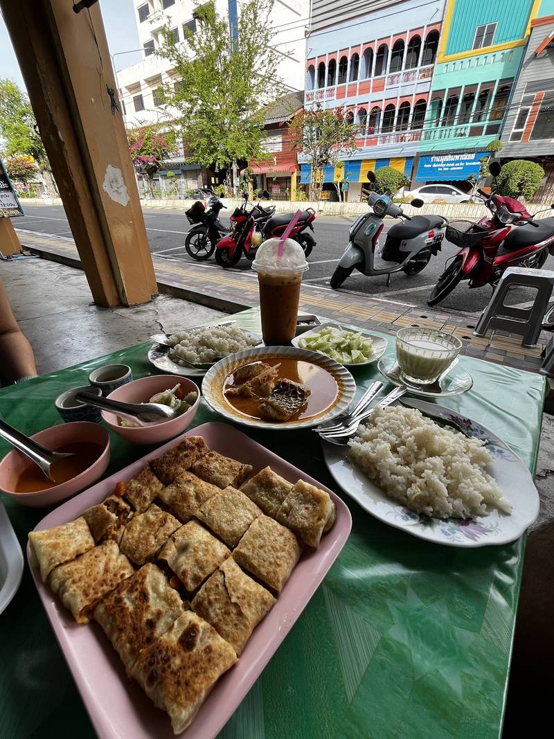 โต๊ะมื้อเช้าหน้าร้าน มีโรตี เครื่องดื่ม มองเห็นถนนในเมืองสตูล